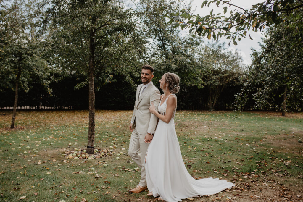 Lachend bruidspaar op een grasveld omringd door fruitbomen
